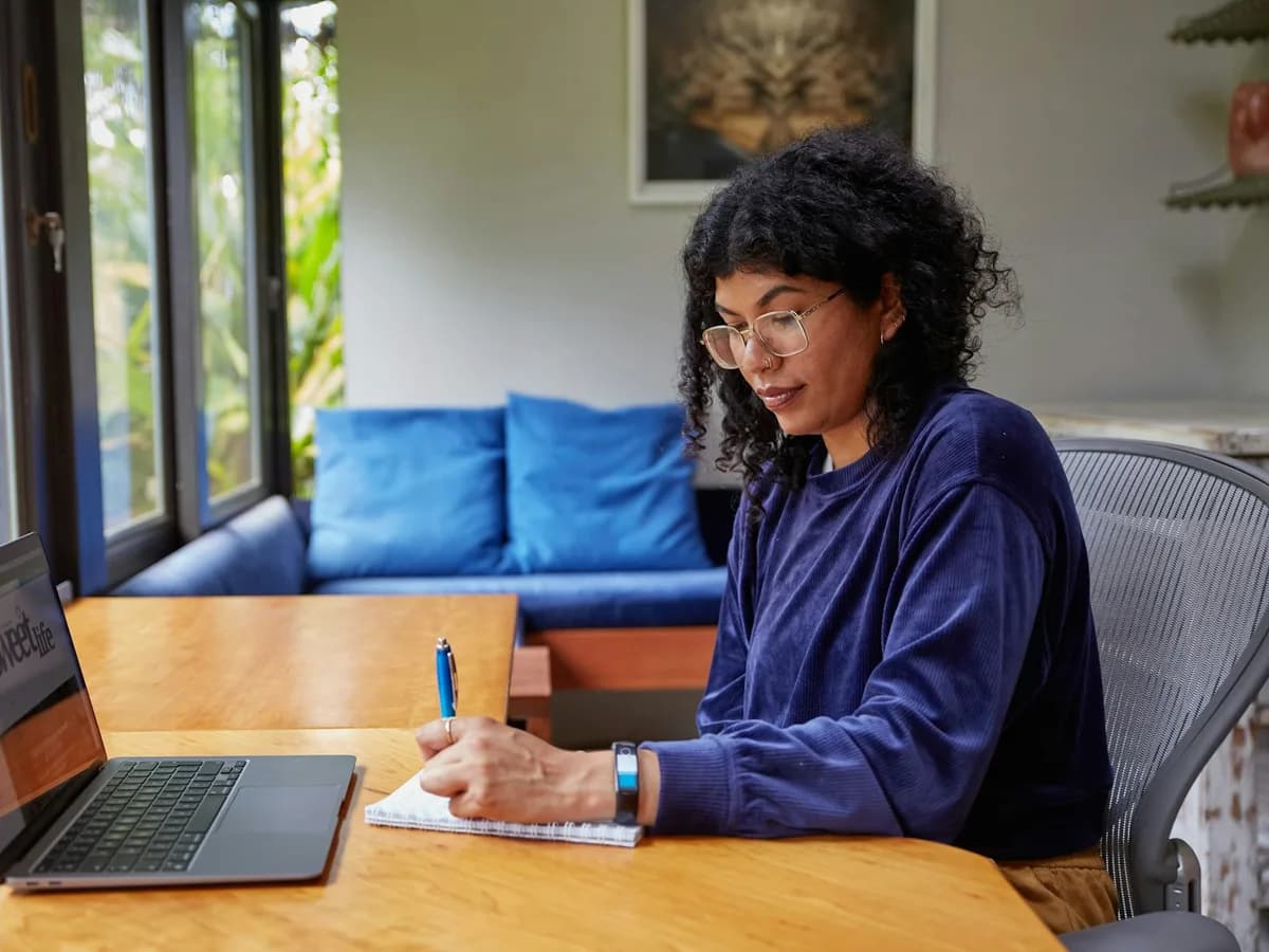 An educator writing notes beside a laptop at home