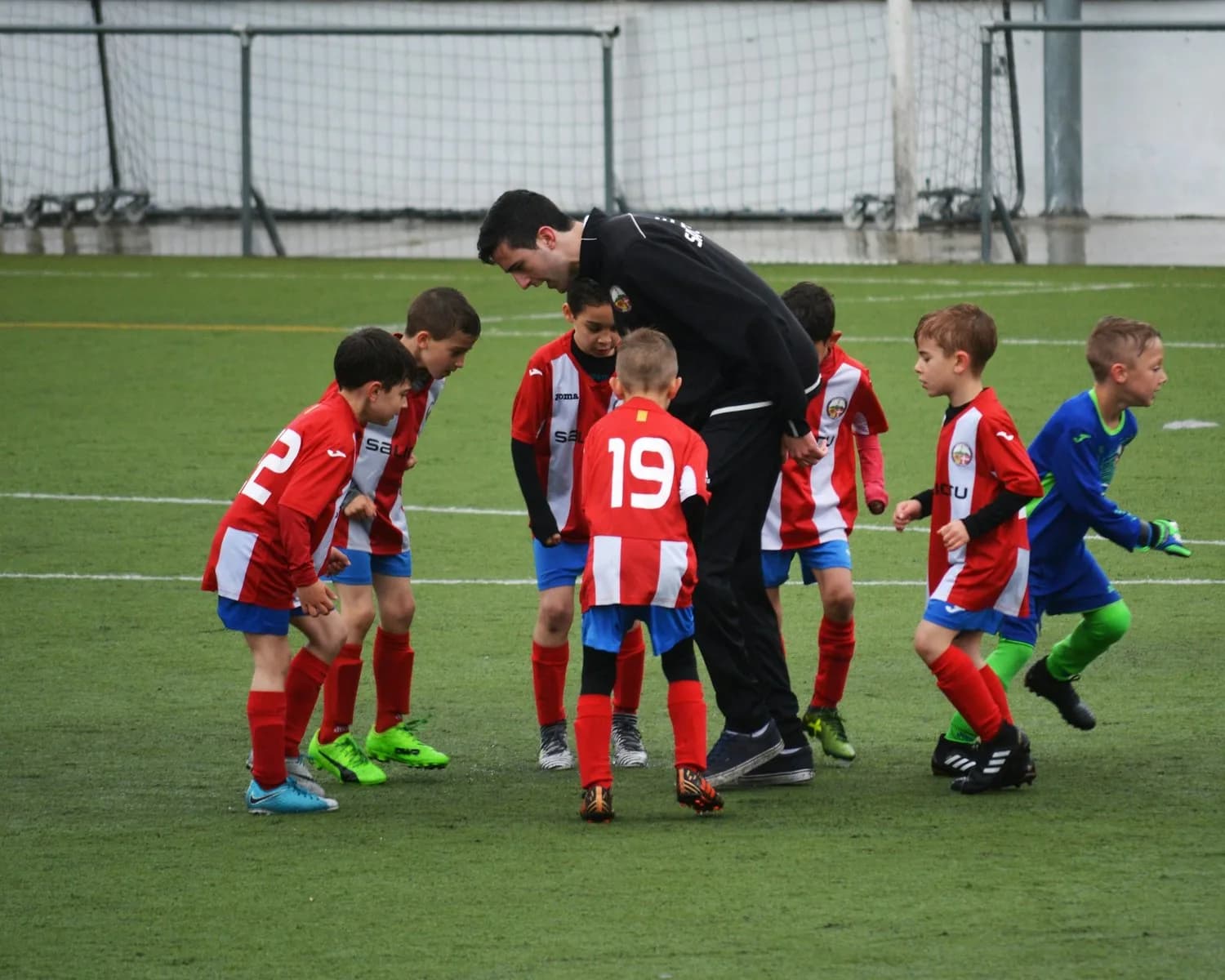 A football coach talking to a group of young players on the pitch