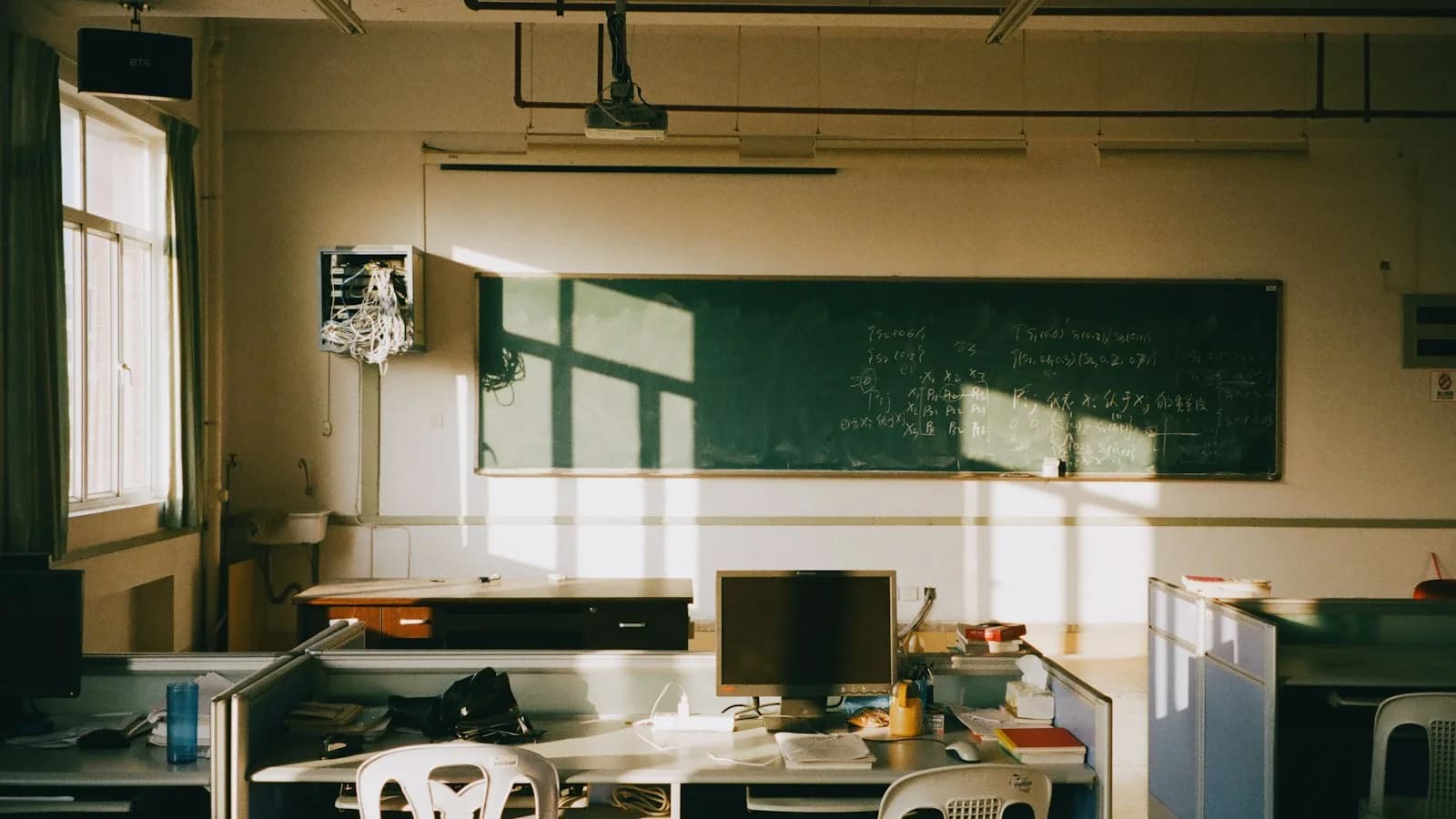 Sunlit empty classroom with a chalkboard and a teacher’s desk