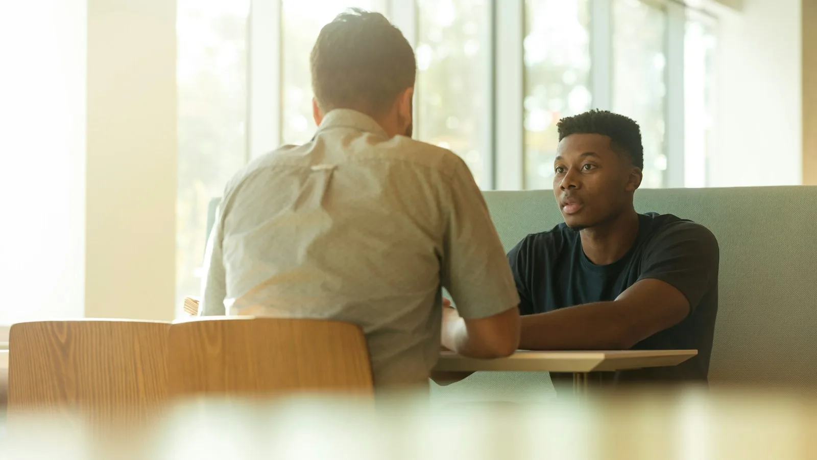 Two colleagues in conversation at a table by a window