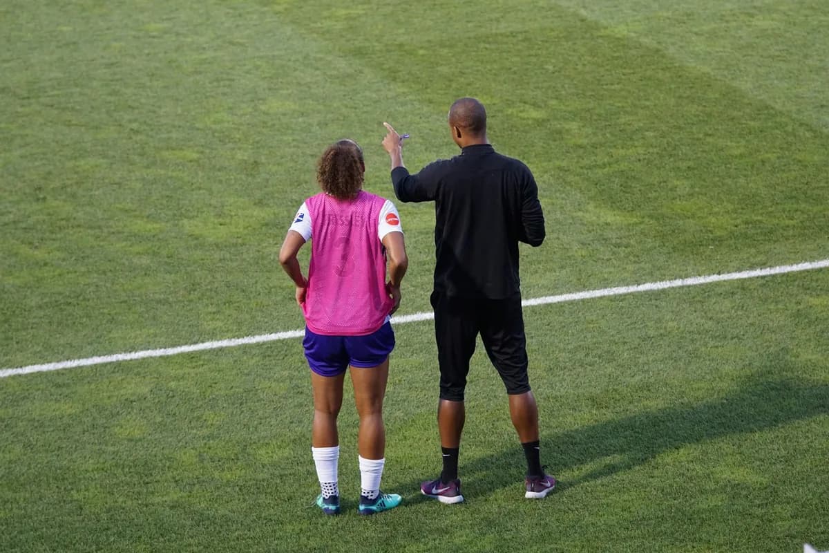A coach giving instructions to a player on a football pitch