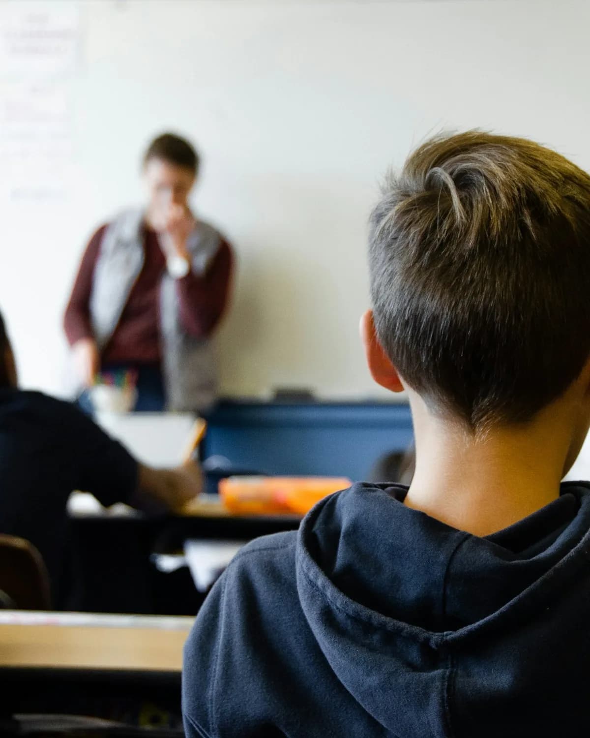 A secondary pupil listening to his teacher at the front of the classroom